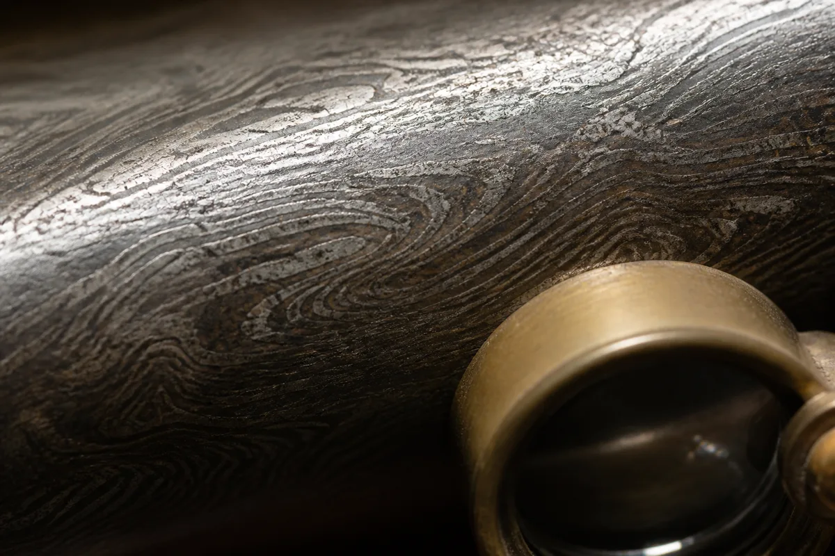 Détail macro d’un canon damassé montrant les moirures du métal en lumière rasante